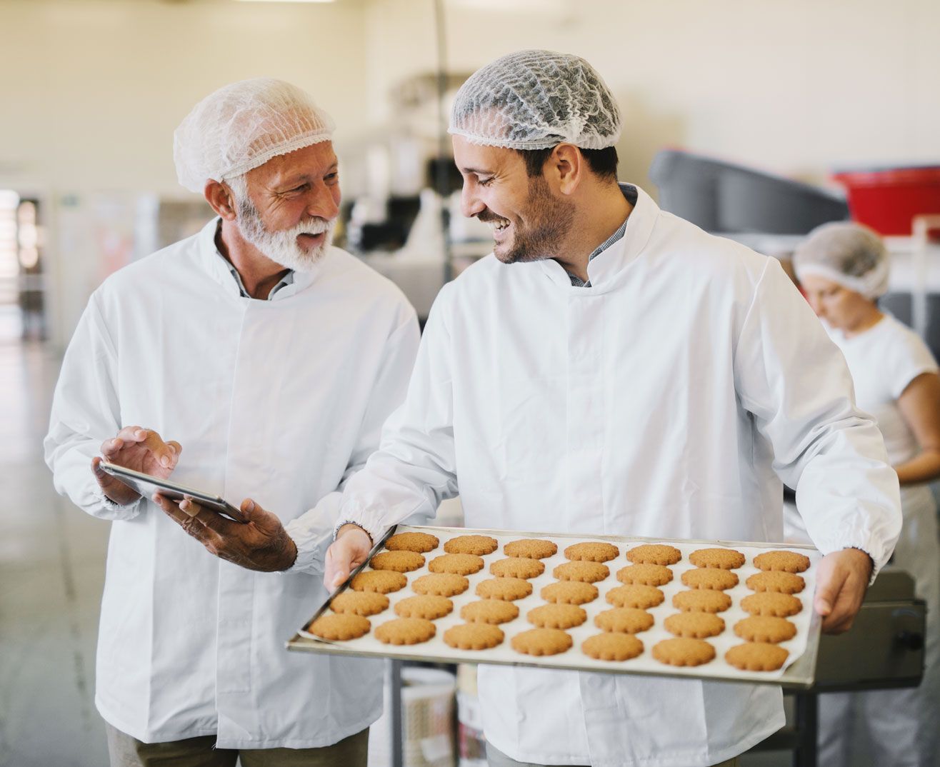 Bakers having a discussion whilst holding a tray of biscuits